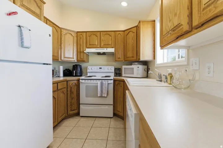 Kitchen featuring light wood cabinetry, white appliances, durable countertops, a double basin sink, and tile flooring