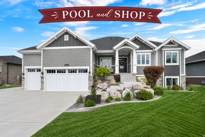 Modern ranch-style home featuring gray siding, stone accents, a three-car garage, manicured front lawn, and a welcoming covered entry