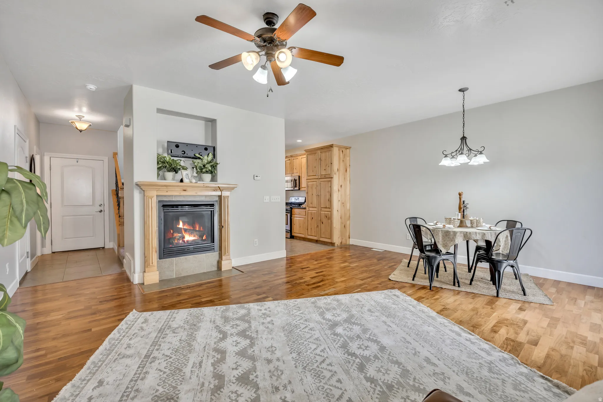 Open-concept living space with wood-finish flooring, a built-in fireplace featuring a light wood mantel, and a ceiling fan with integrated lighting