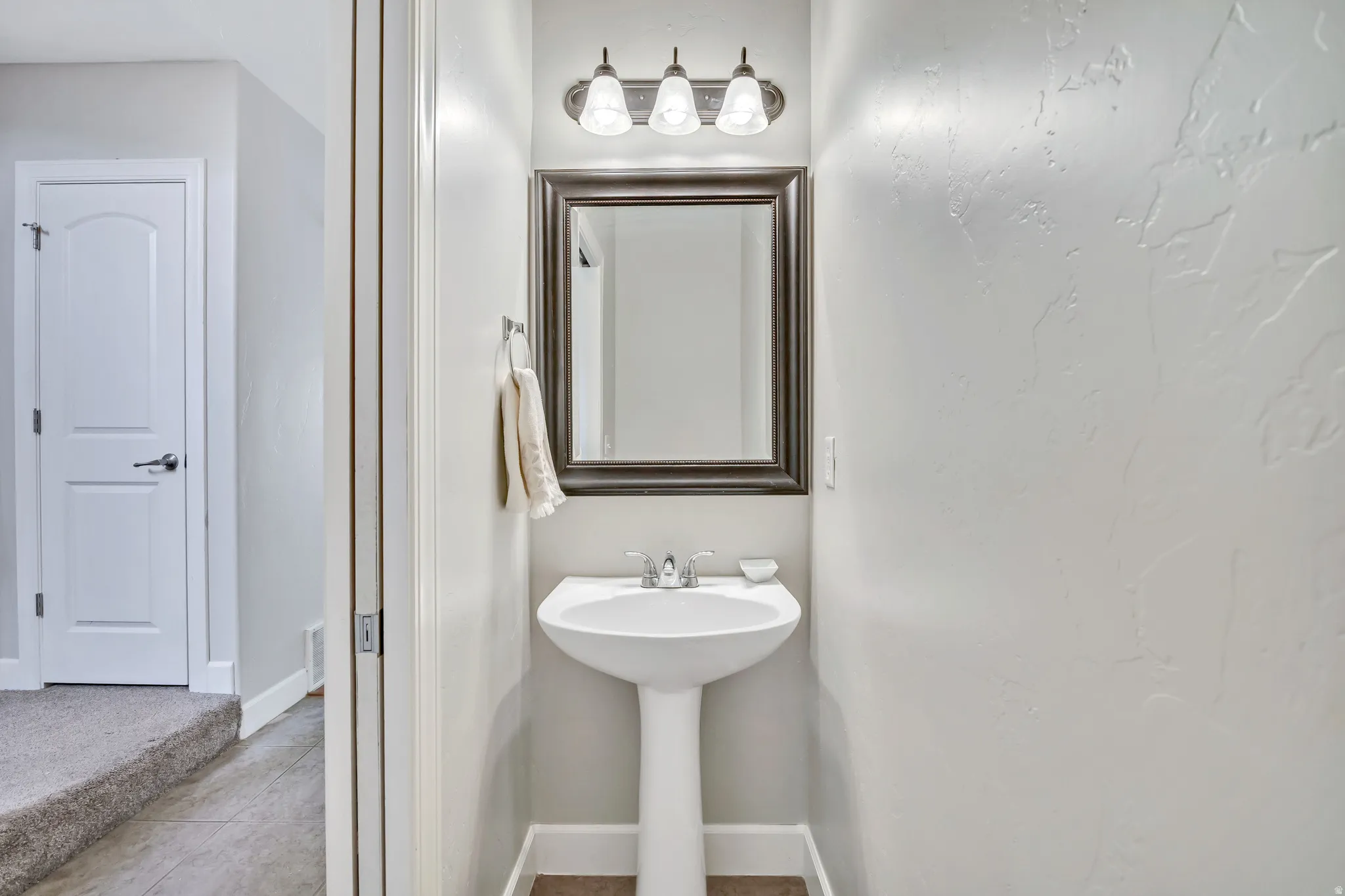 Pedestal sink with chrome faucet, framed mirror, and three-light vanity fixture