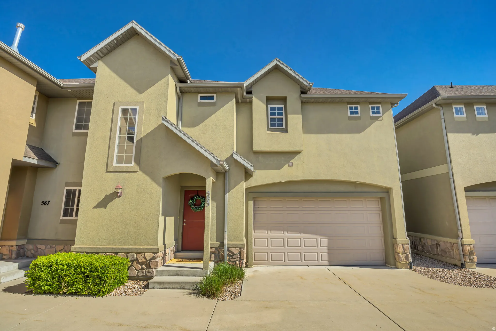 Stucco exterior with stone accents, a concrete driveway, an attached garage, a covered entry, and a red front door