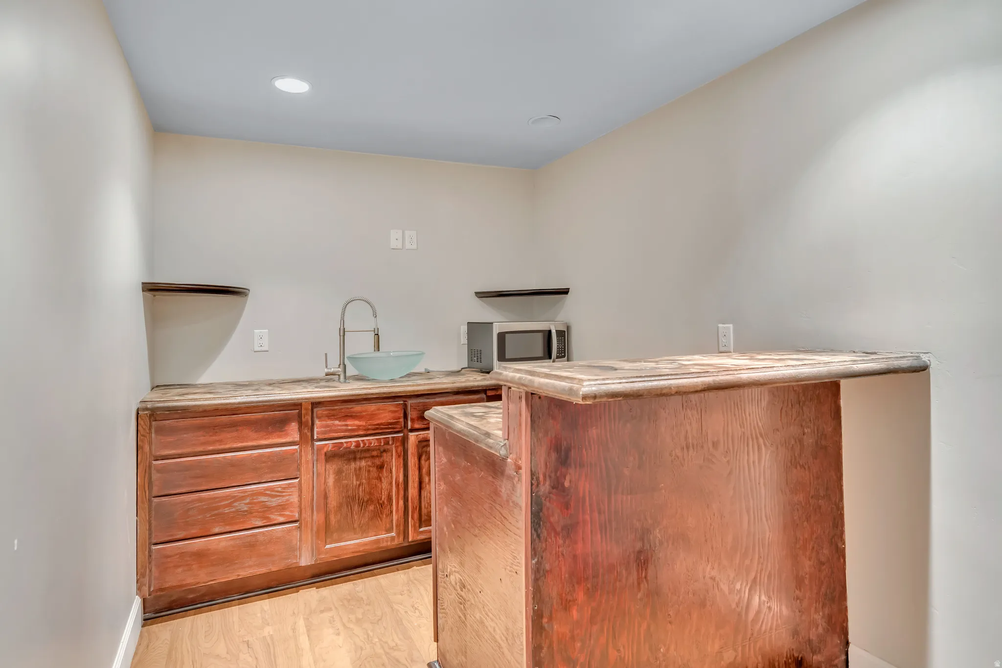 Wet bar featuring wood cabinetry, stone-finish countertops, a vessel sink with a gooseneck faucet, a built-in bar extension, and recessed lighting