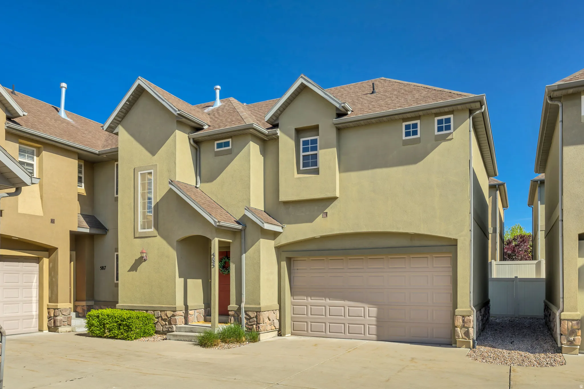 Stucco exterior residence with an attached garage, featuring a covered entryway, stone accents at the base, and multiple windows with white trim