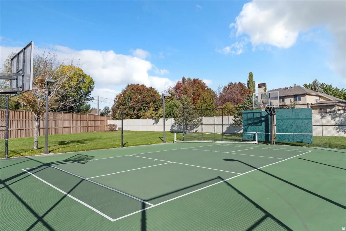 Multi-sport court featuring a basketball hoop and net, surrounded by a manicured lawn and perimeter fencing