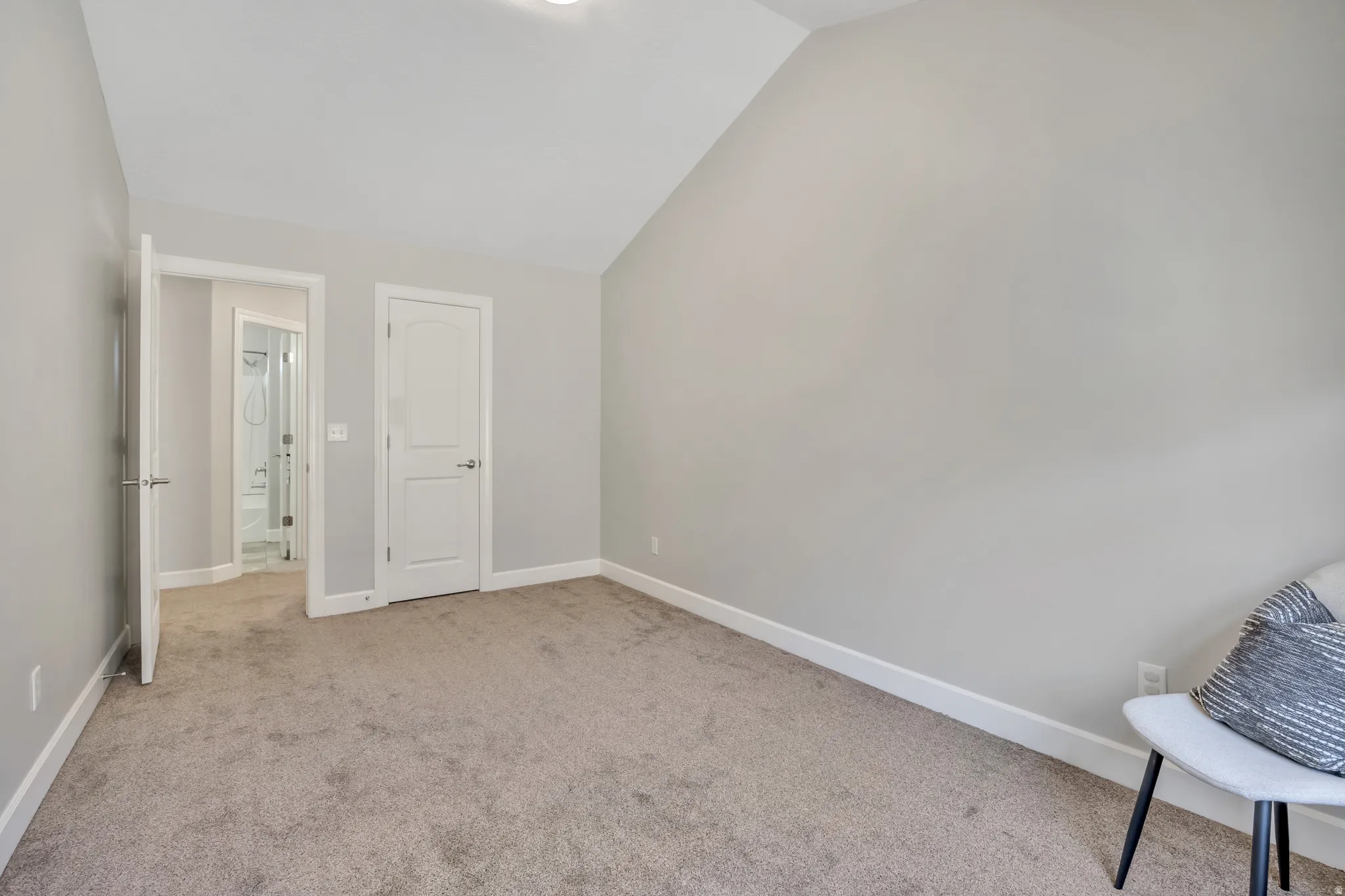 Carpeted room featuring a vaulted ceiling, neutral wall paint, white trim, and a paneled interior door with brushed nickel hardware