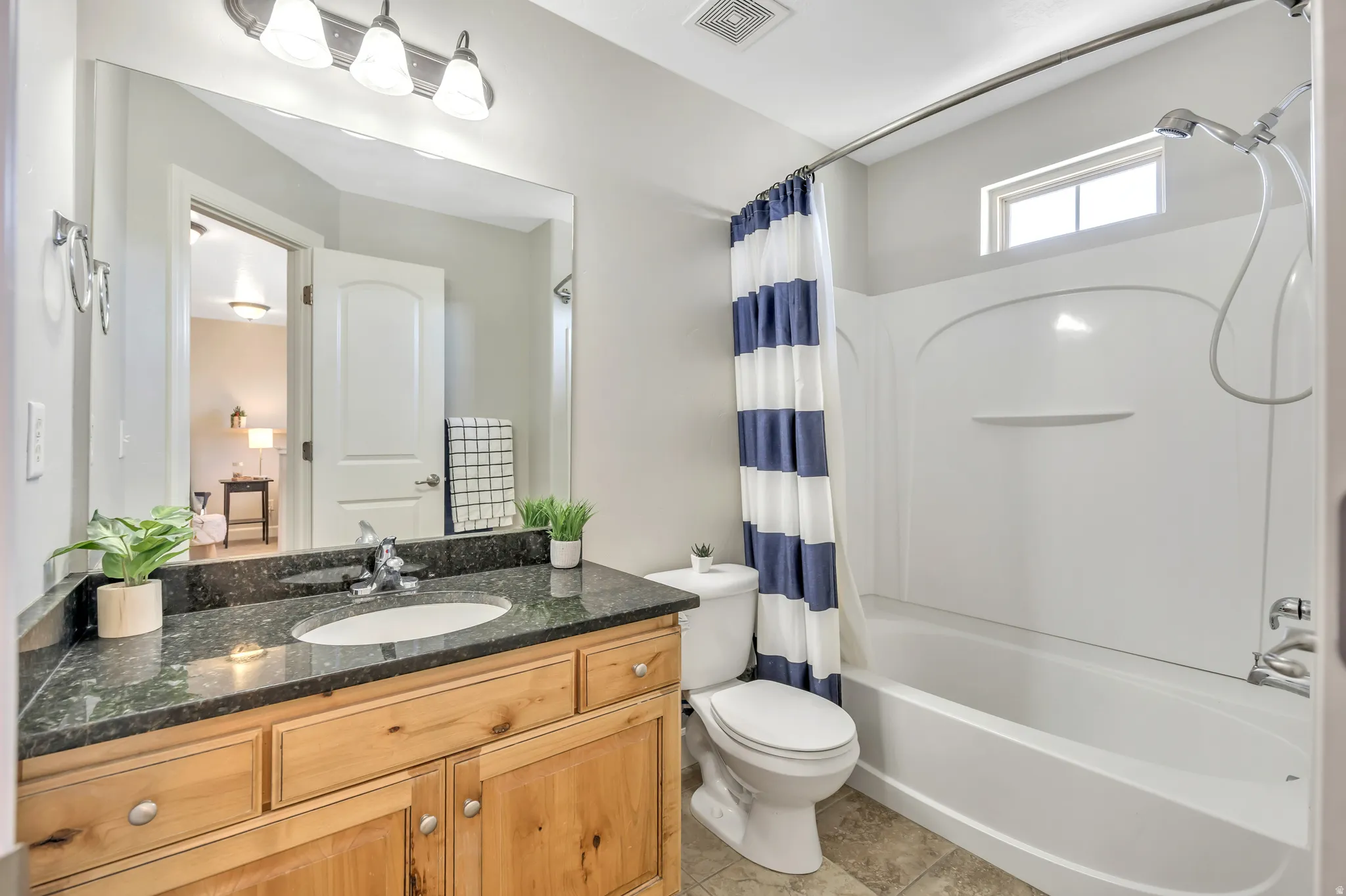 Bathroom featuring a wood-finish vanity with a dark speckled countertop, an undermount sink, and a large wall-mounted mirror