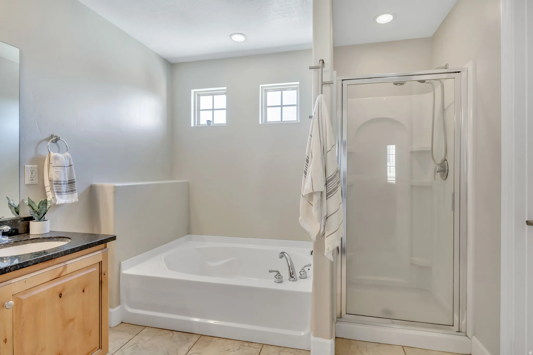 Bathroom featuring a built-in soaking tub, glass-enclosed shower, light wood-finish vanity with a dark countertop, and recessed lighting