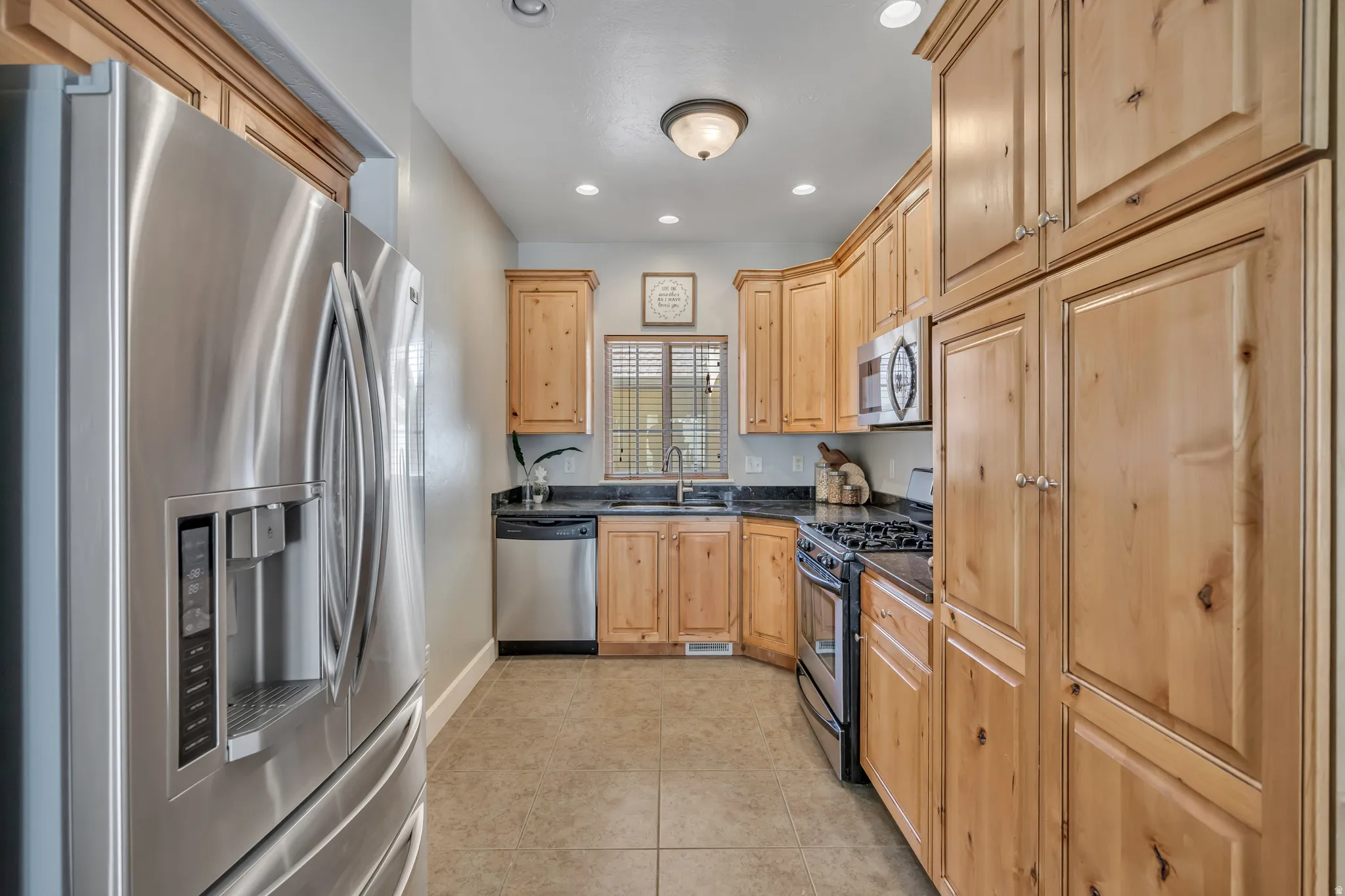 Galley kitchen featuring stainless steel appliances, natural wood cabinetry, a built-in oven with a gas cooktop, and a tile floor