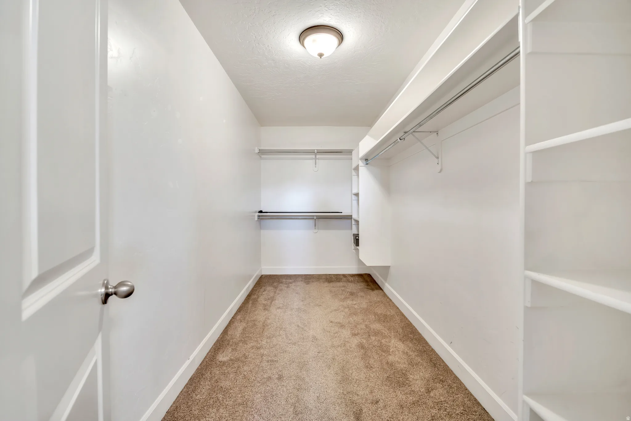 Spacious walk-in closet featuring white shelving units, multiple hanging rods, recessed lighting, and soft carpet flooring