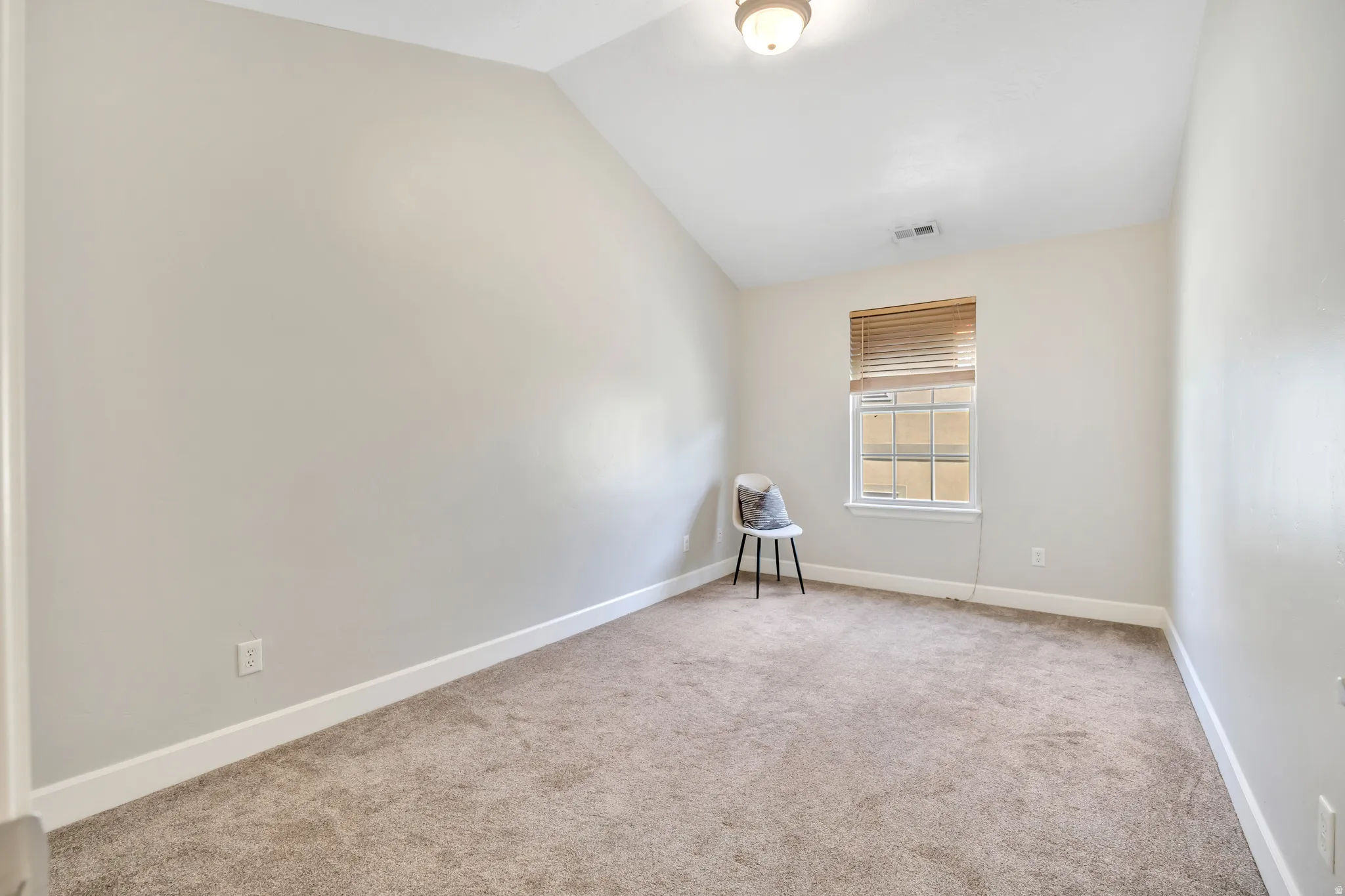 Spacious room featuring vaulted ceilings, neutral-toned carpeting, and a single window with wooden blinds
