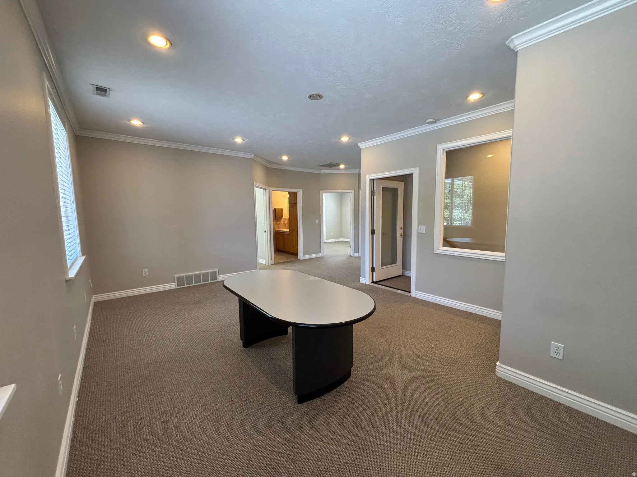 Carpeted office area featuring recessed lighting, crown molding, a window with blinds, and a glass-paneled door