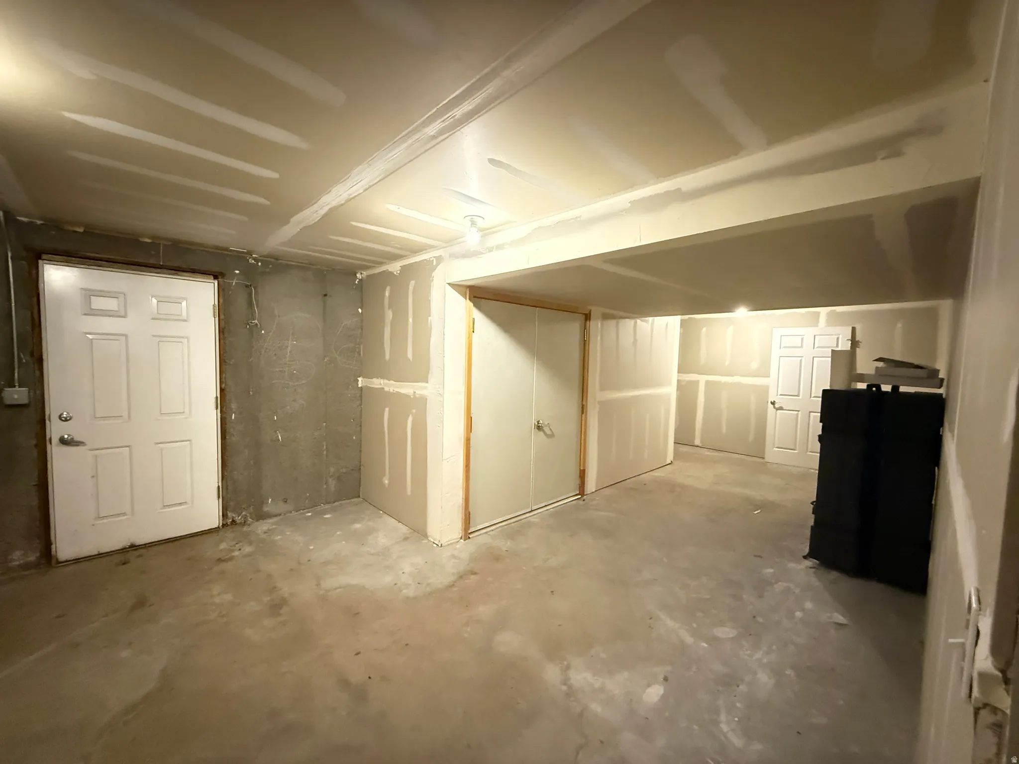 Unfinished lower level featuring exposed concrete walls and floor, drywall installed on perimeter walls and ceiling, and multiple panel doors