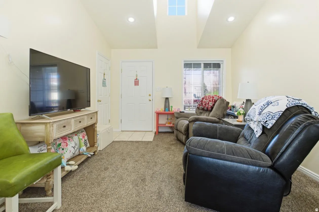 Carpeted living area featuring vaulted ceilings, recessed lighting, and a front entry door with an adjacent window