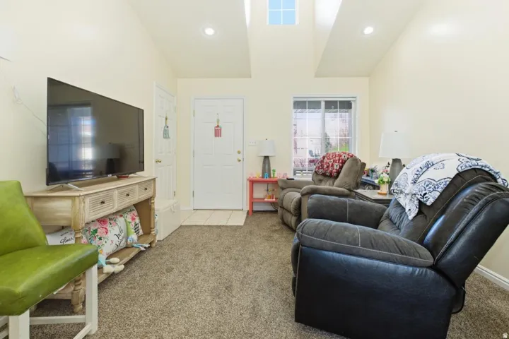 Carpeted living area featuring vaulted ceilings, recessed lighting, and a front entry door with an adjacent window