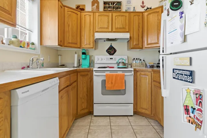 Kitchen featuring wood cabinetry, a white countertop, a double basin sink, white appliances, and ceramic tile flooring