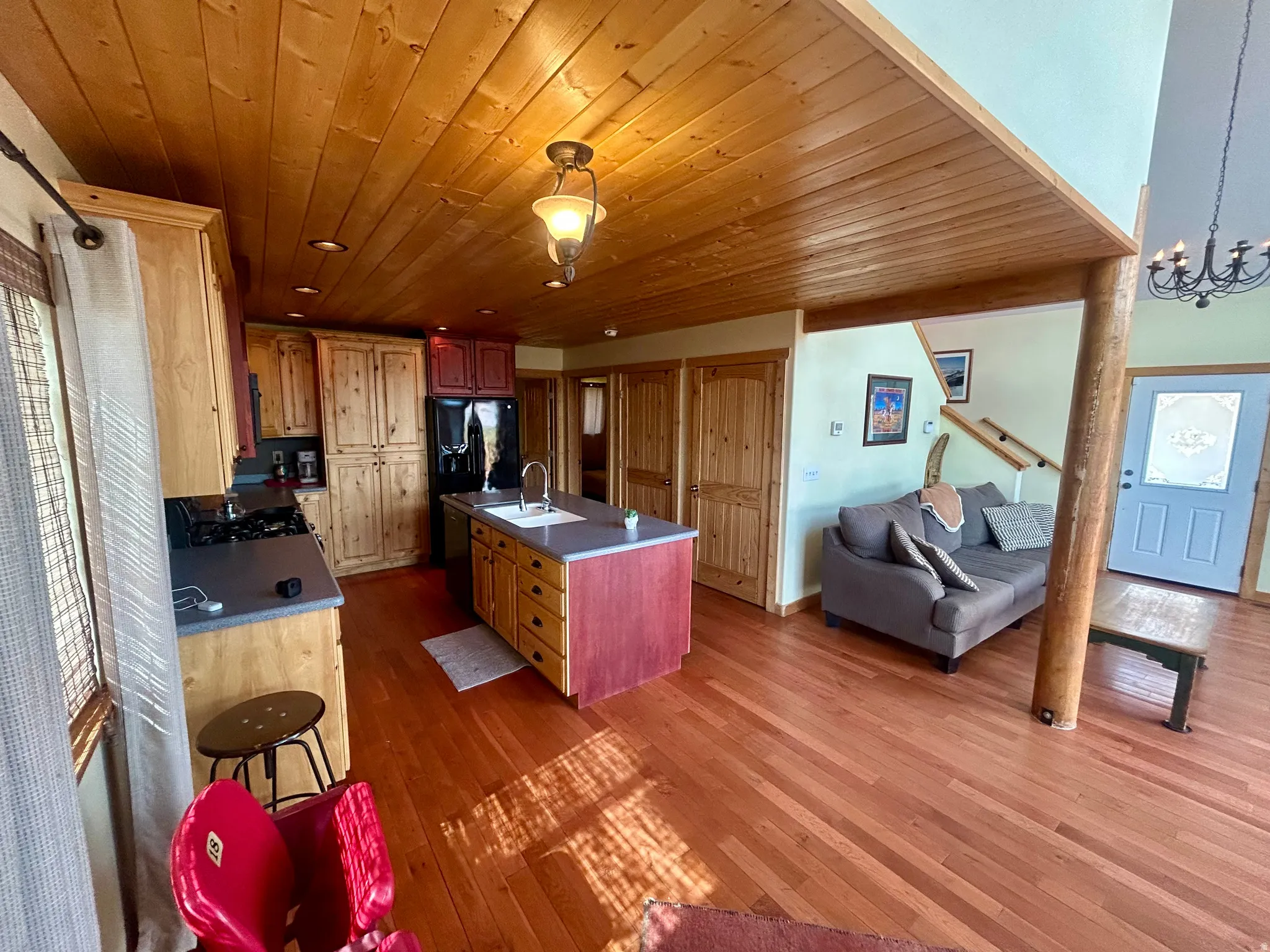 Open-concept kitchen and living area featuring wood-finish flooring, a wood plank ceiling, and a kitchen island with a built-in sink