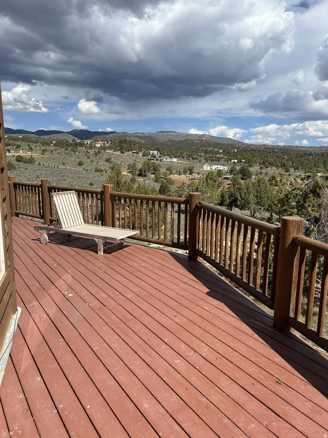 Expansive outdoor deck with red-stained wood flooring and natural log railing