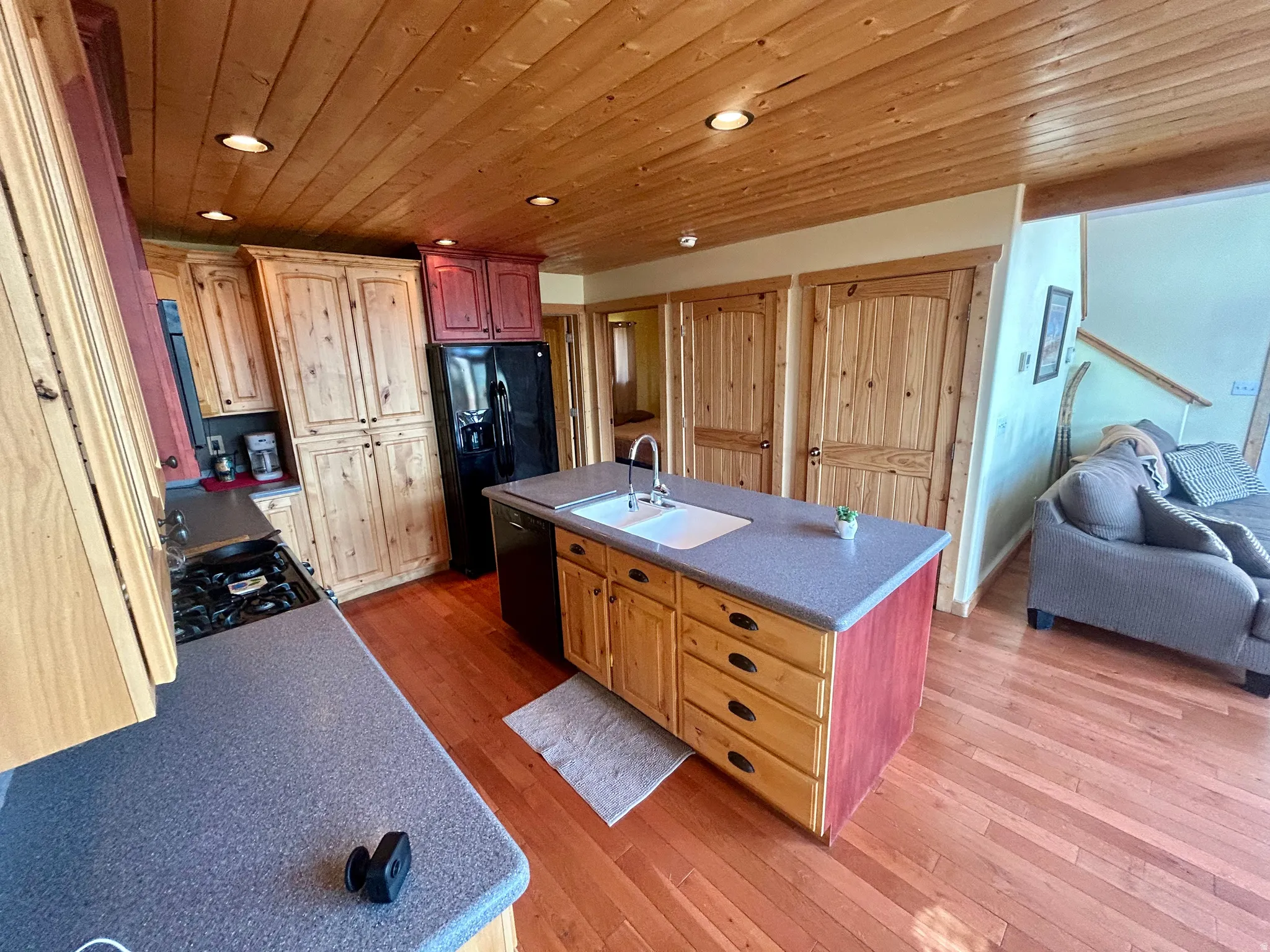 Kitchen featuring wood-finish cabinetry, a black gas range, built-in black refrigerator, and an island with an integrated sink