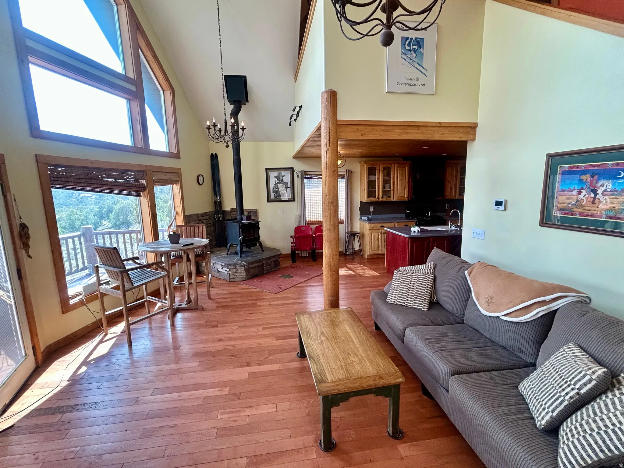 Open-concept living space featuring hardwood flooring, a prominent wood-burning stove with a stone hearth, and a kitchen with wood cabinetry and an island