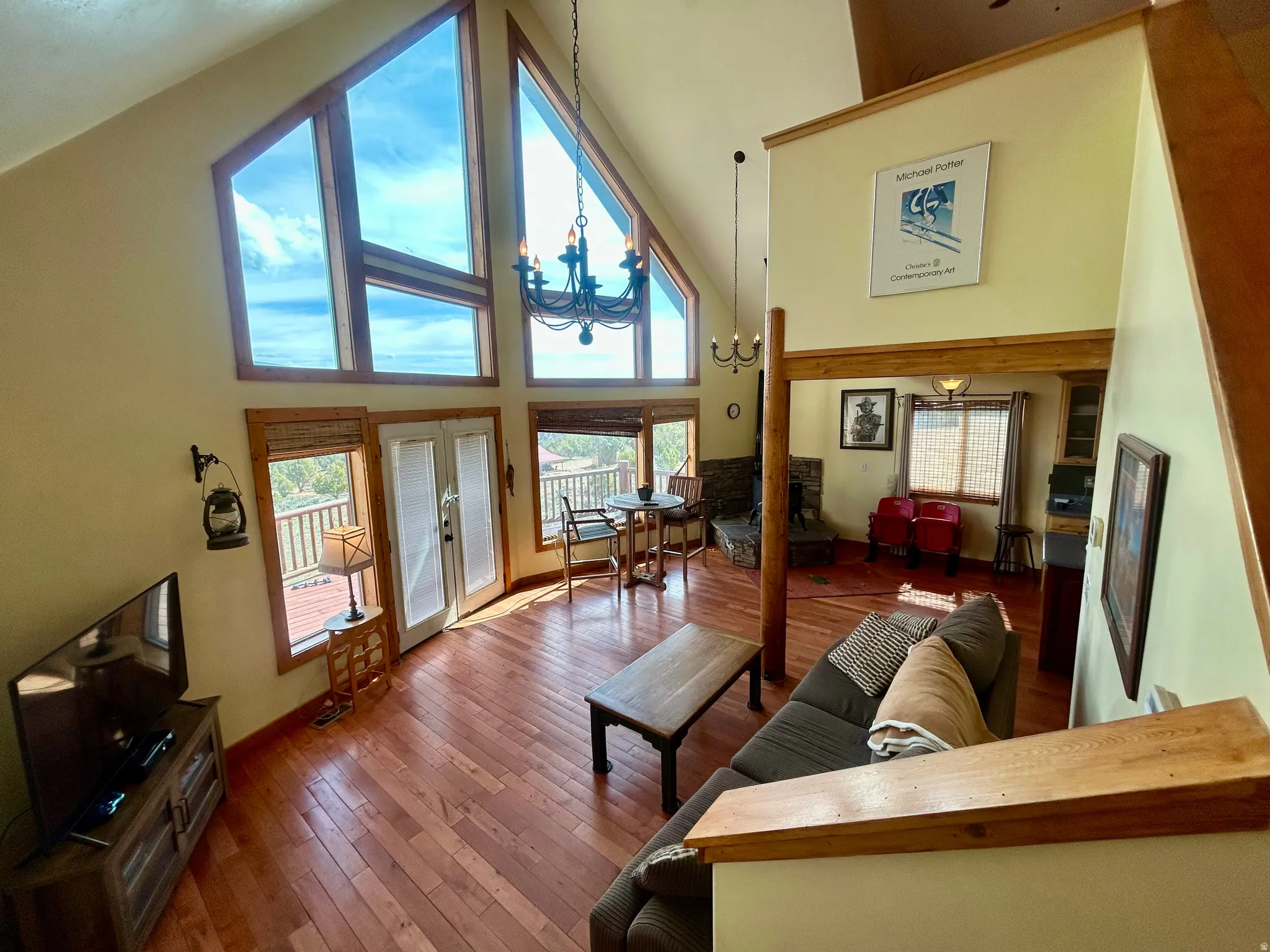 Vaulted ceiling living area featuring large picture windows, wood-finish flooring, a wrought iron chandelier, and direct access to an outdoor deck