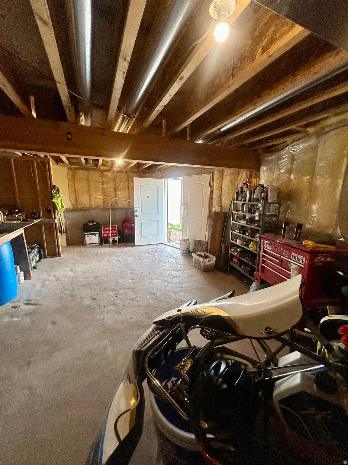Unfinished basement with concrete flooring, exposed wood beam ceiling, exposed ductwork, and double panel doors