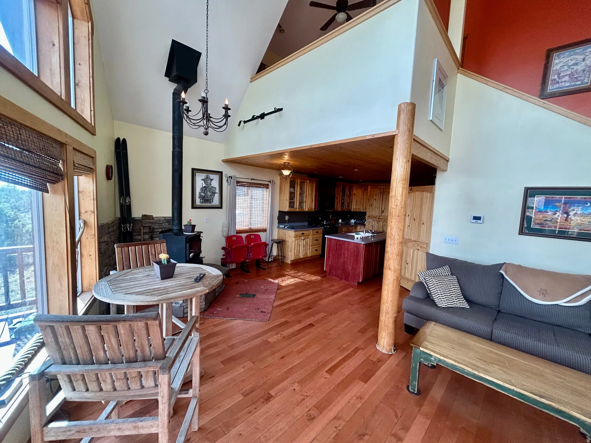 Spacious open-concept living area featuring high vaulted ceilings, warm wood-finish flooring, and a prominent wood-burning stove with a stone surround