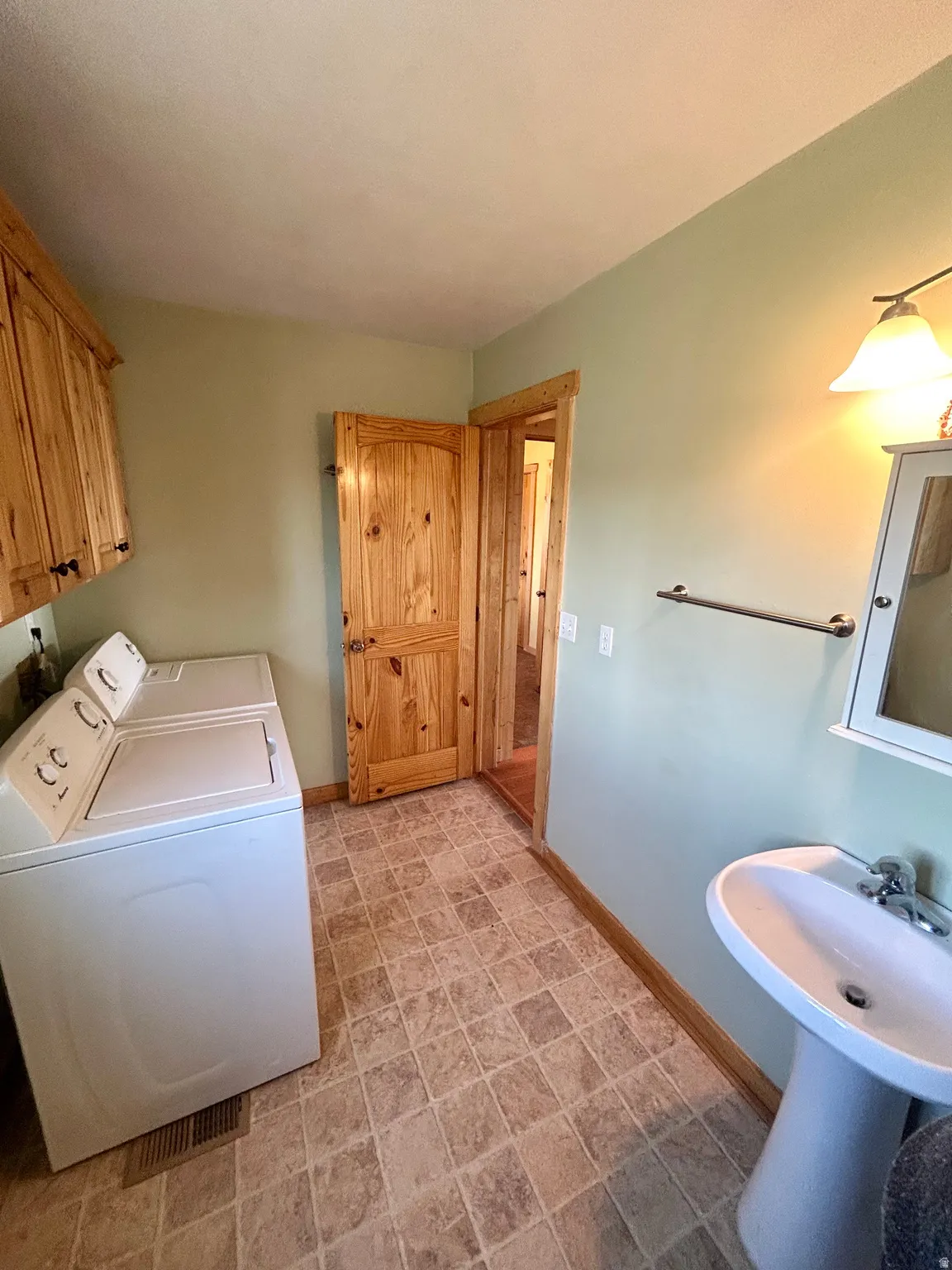 Laundry area featuring a pedestal sink, wood-finish cabinetry, and patterned tile flooring
