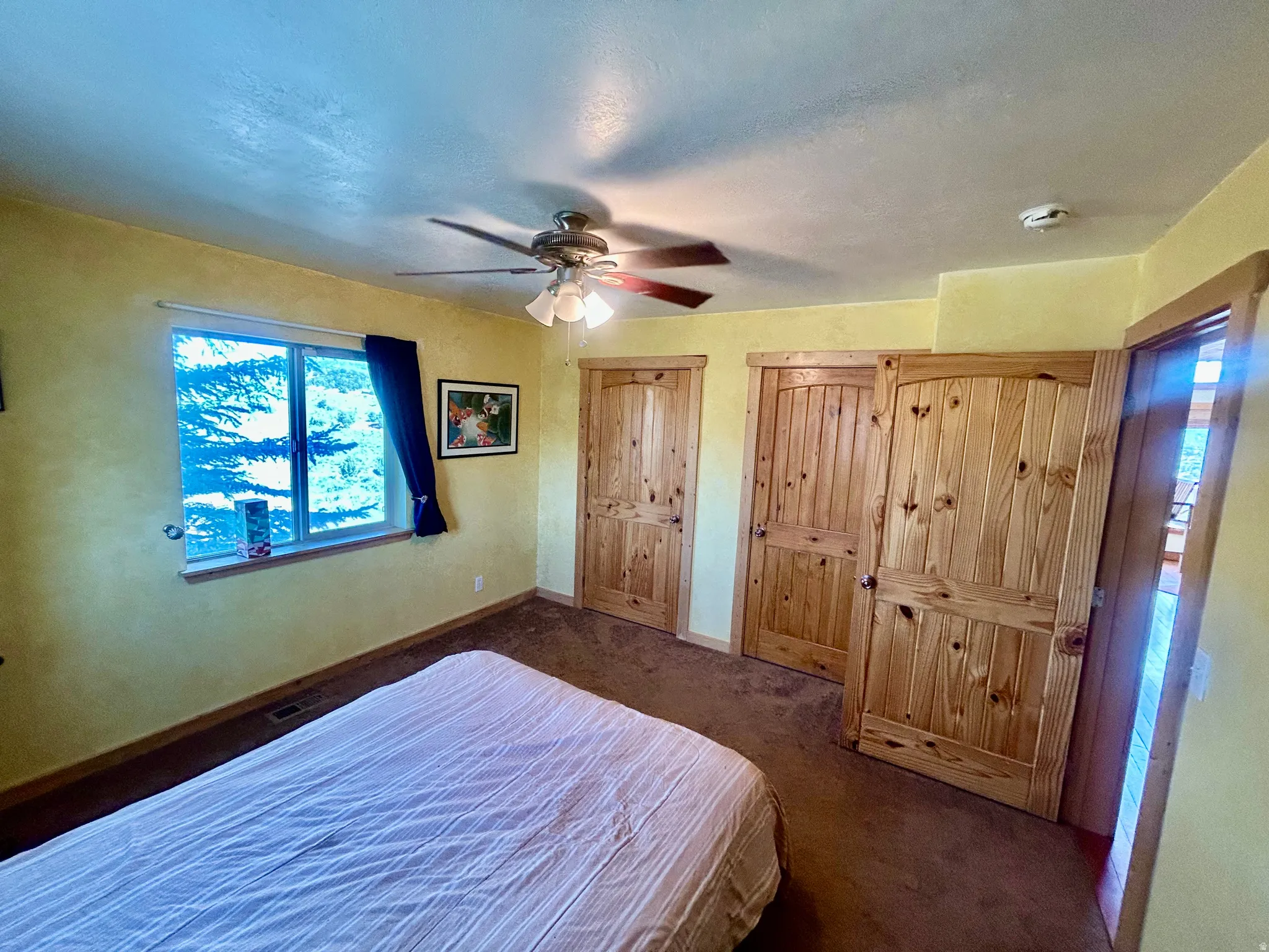 Main Level Bedroom featuring a window with exterior tree scenery, three paneled wood-finish doors, and a ceiling fan with light fixture