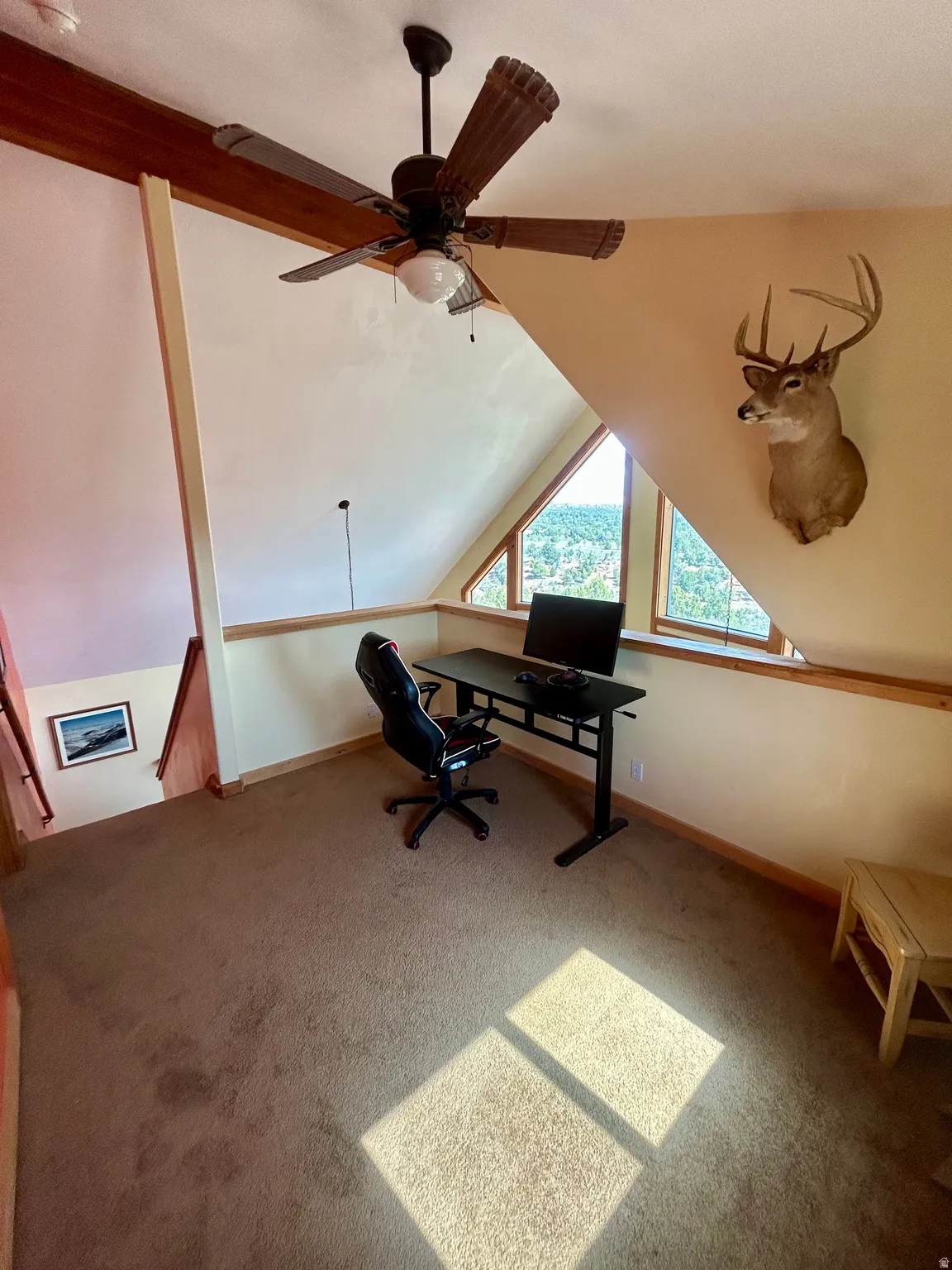 Carpeted loft space featuring an angled ceiling, exposed wood beams, and a ceiling fan with integrated lighting
