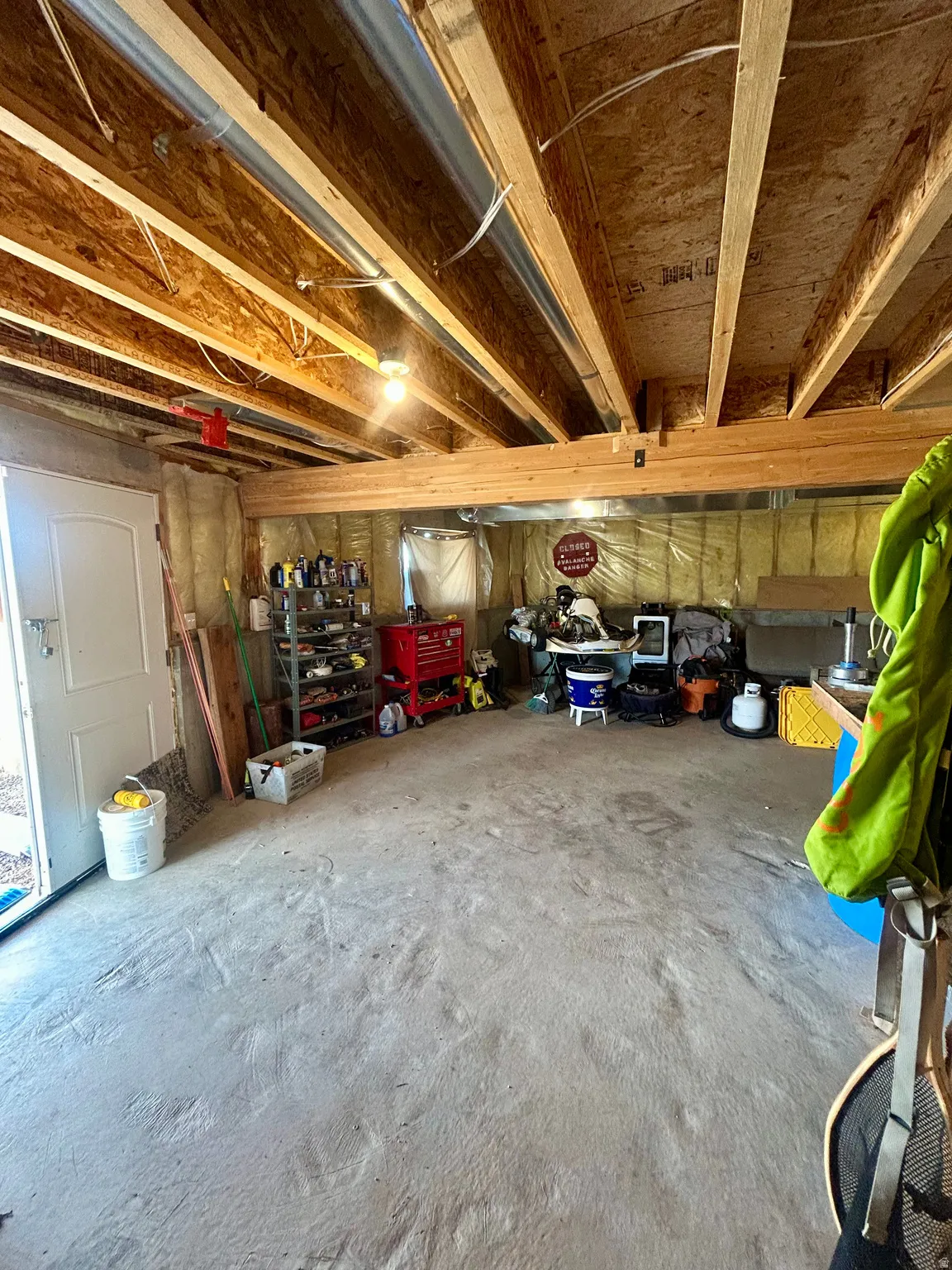 Unfinished basement with exposed wooden joists and subflooring, concrete flooring, and an insulated wall