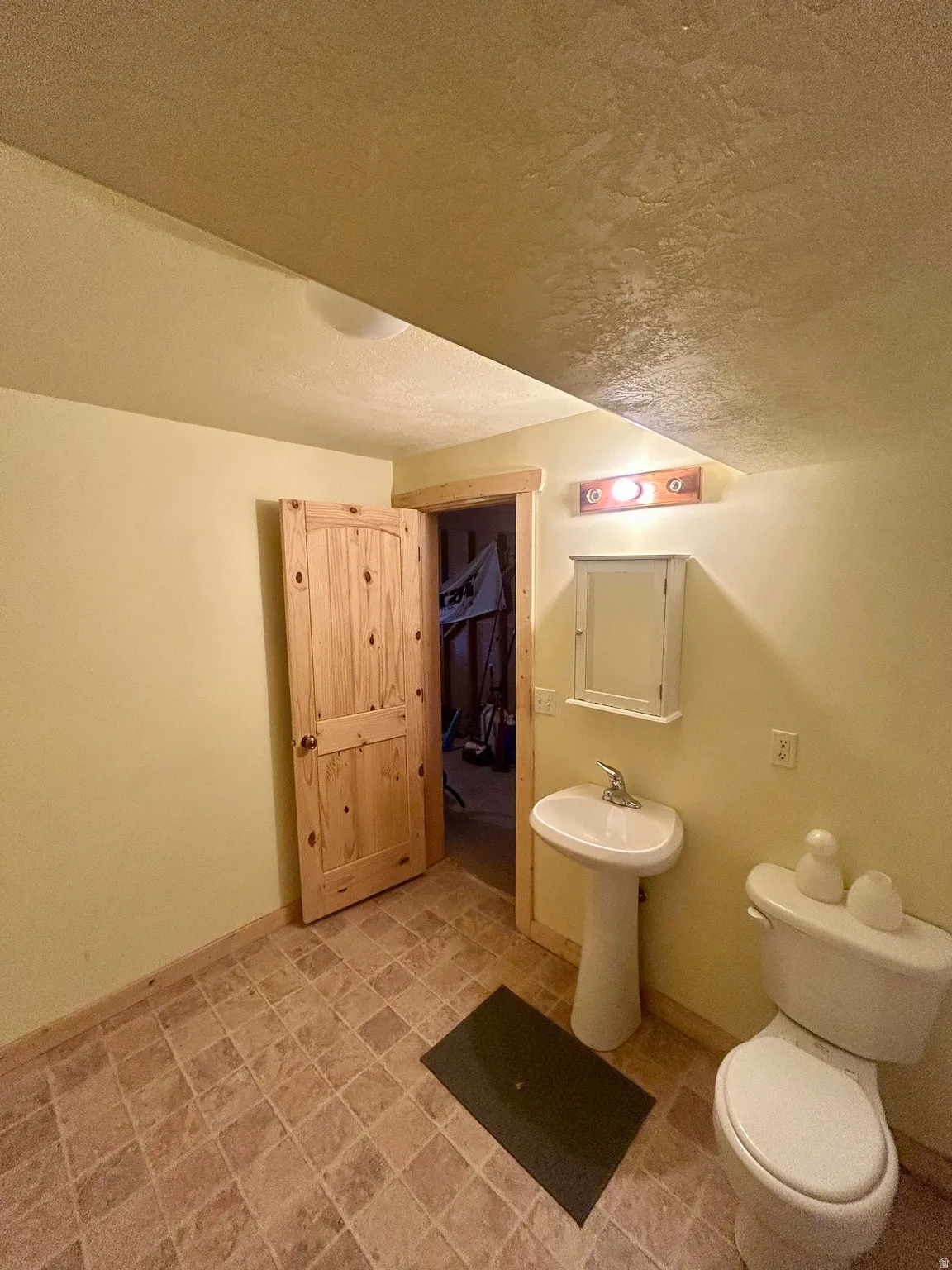 Compact bath featuring a pedestal sink, white toilet, and tile-finish flooring