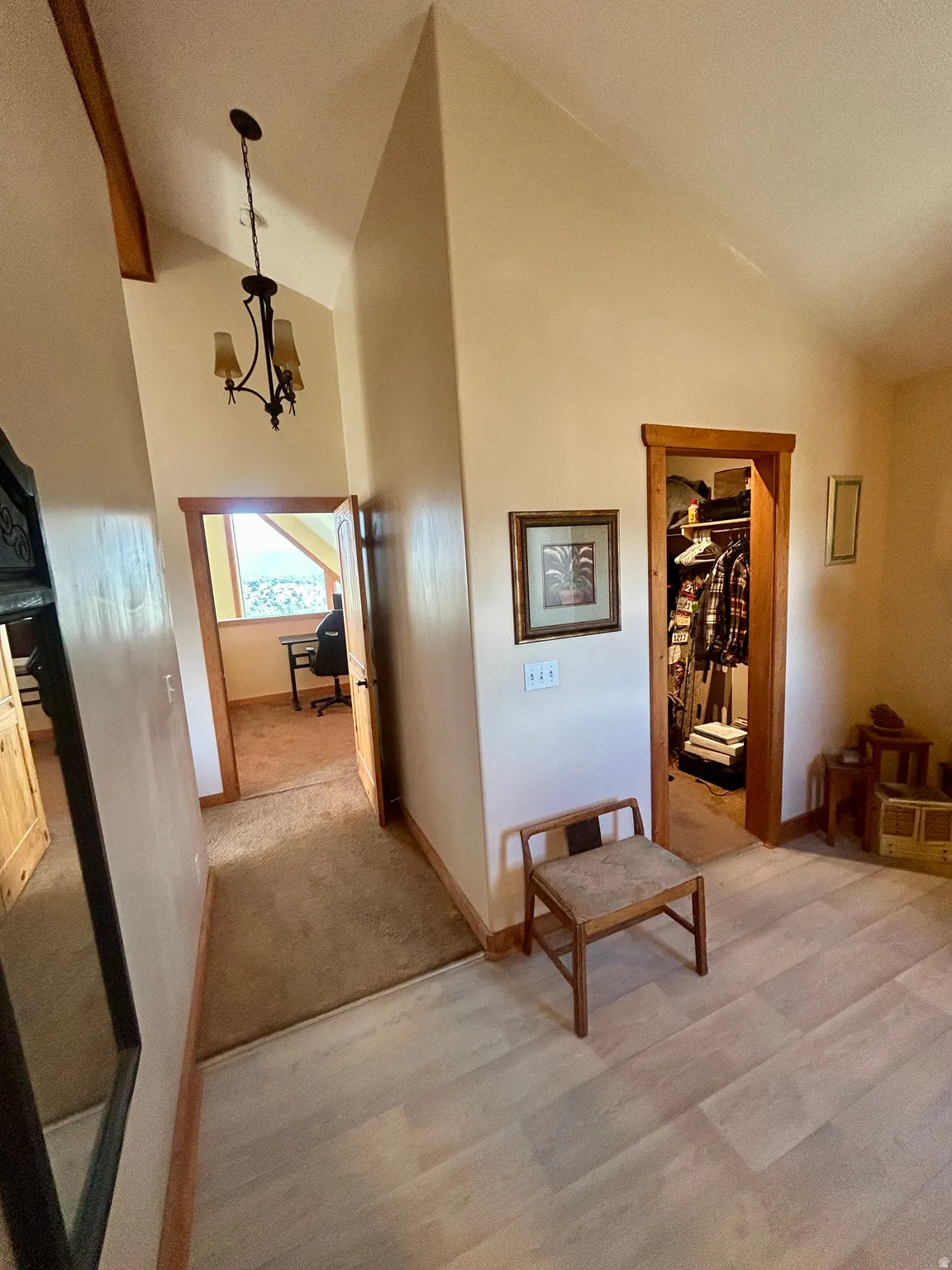 Hallway featuring a vaulted ceiling with a chandelier, wood-finish flooring, and a carpeted section