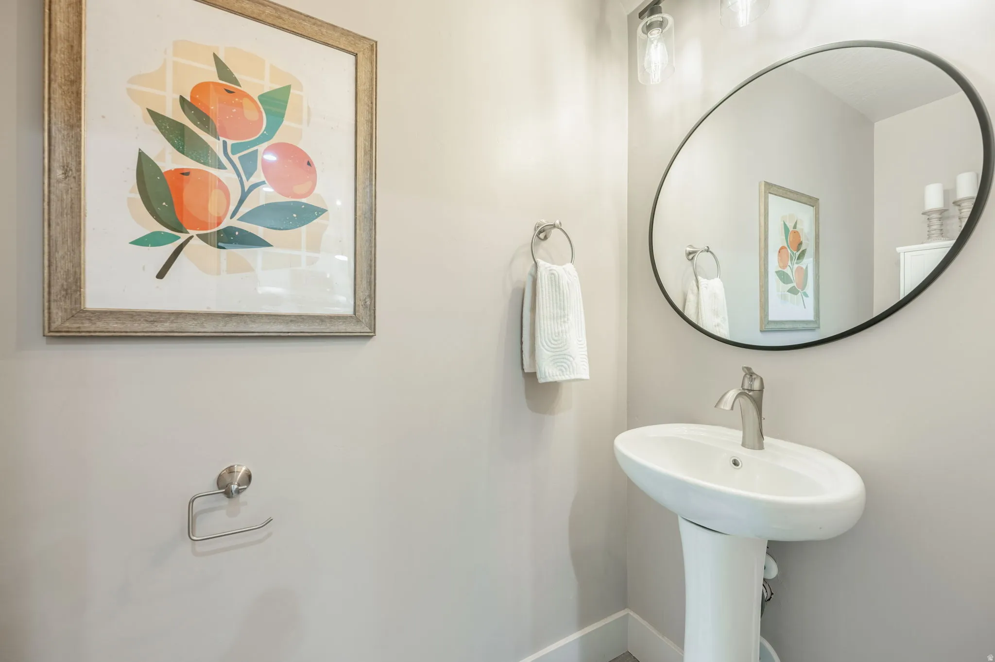 Pedestal sink with a brushed nickel faucet, complemented by a large oval mirror with a black frame and a three-light vanity fixture