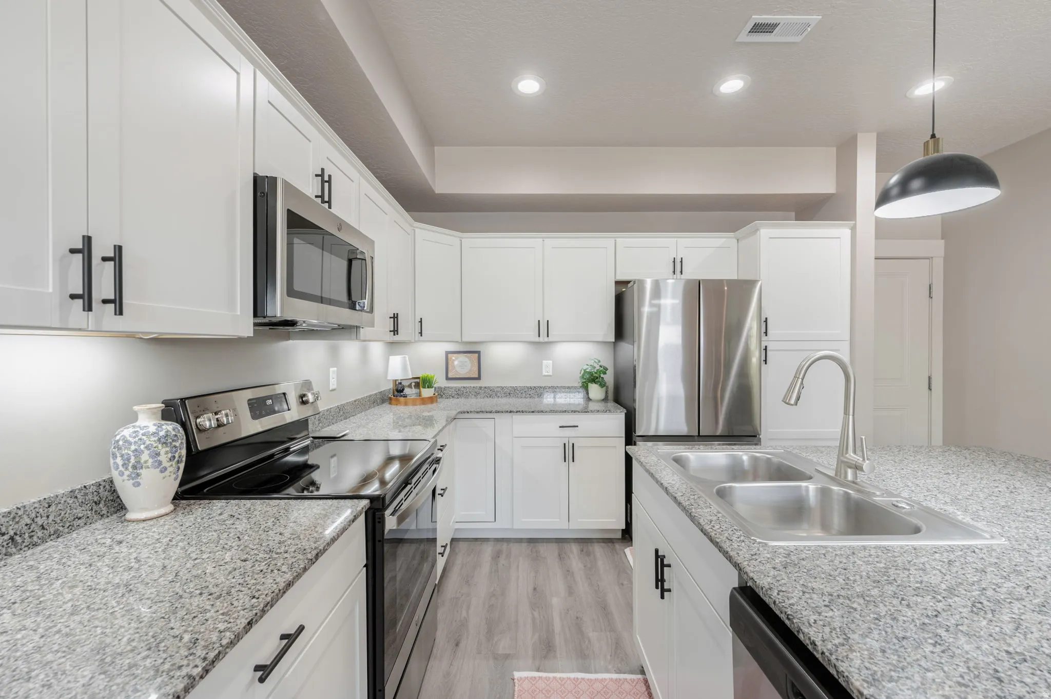 Bright kitchen featuring white shaker cabinetry, stainless steel appliances, speckled stone countertops, and wood-finish flooring