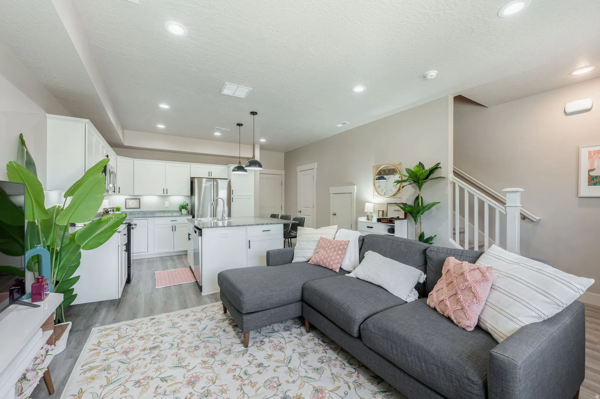 Open-concept living area featuring wood-finish flooring, recessed lighting, and a white staircase with a prominent newel post