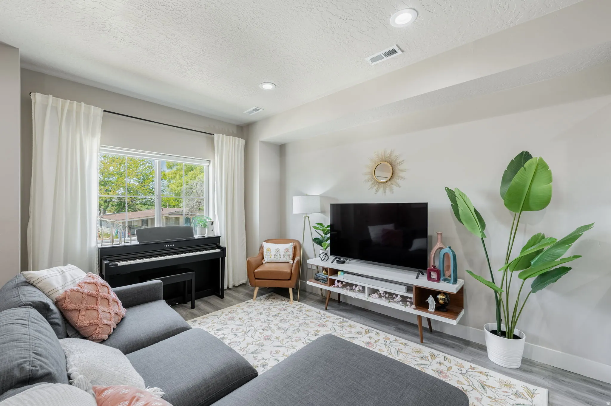 Living area featuring wood-finish flooring, recessed lighting, and a large window with white curtain panels