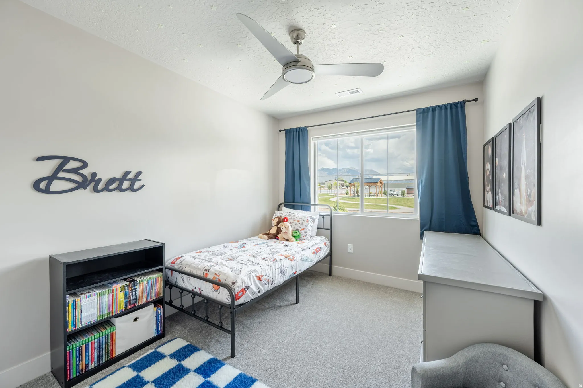 Carpeted room featuring a ceiling fan, a large window with blue drapery, and a built-in shelving unit