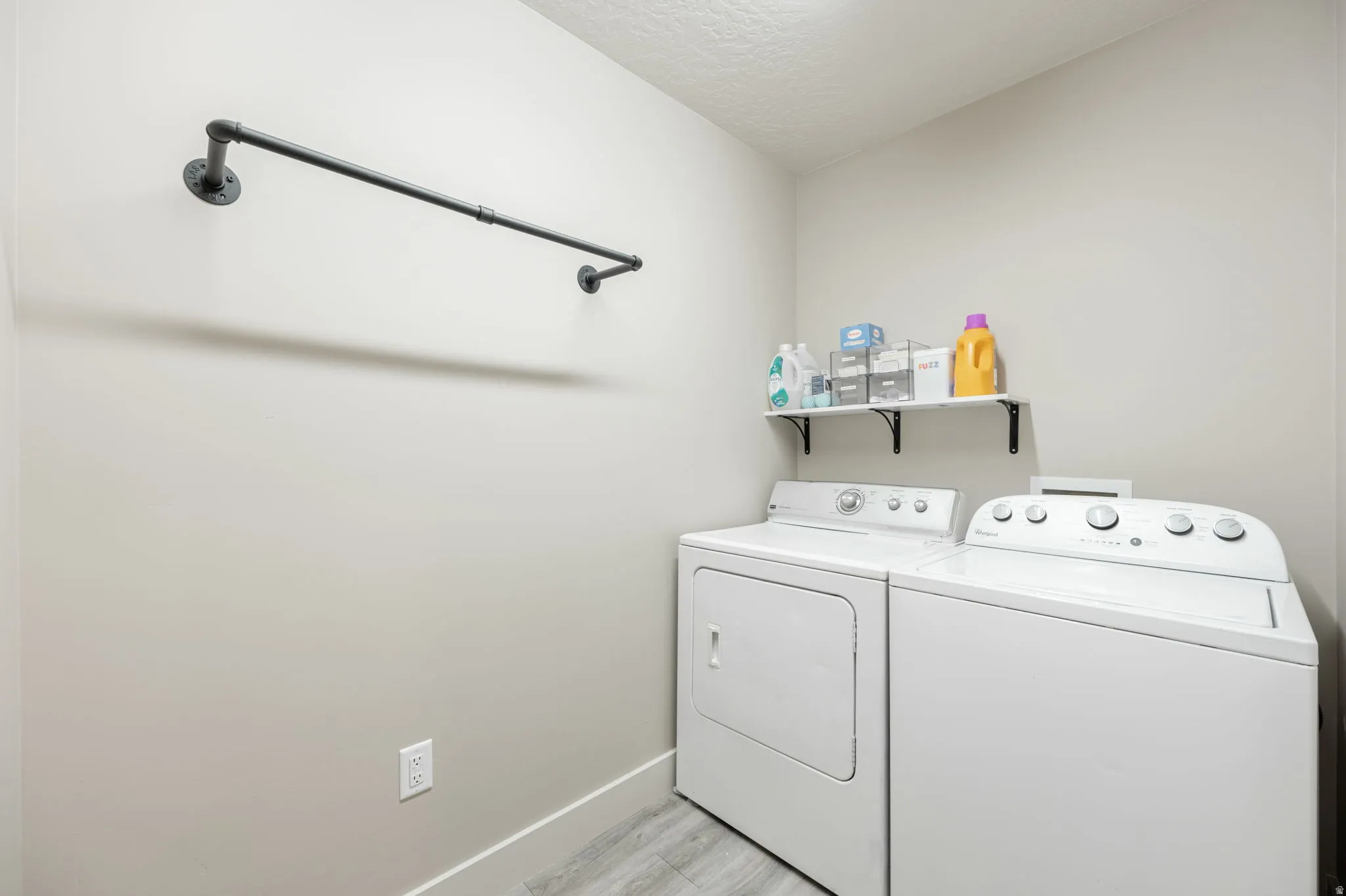 Dedicated laundry area featuring a wall-mounted drying rod, floating shelf, and wood-finish flooring