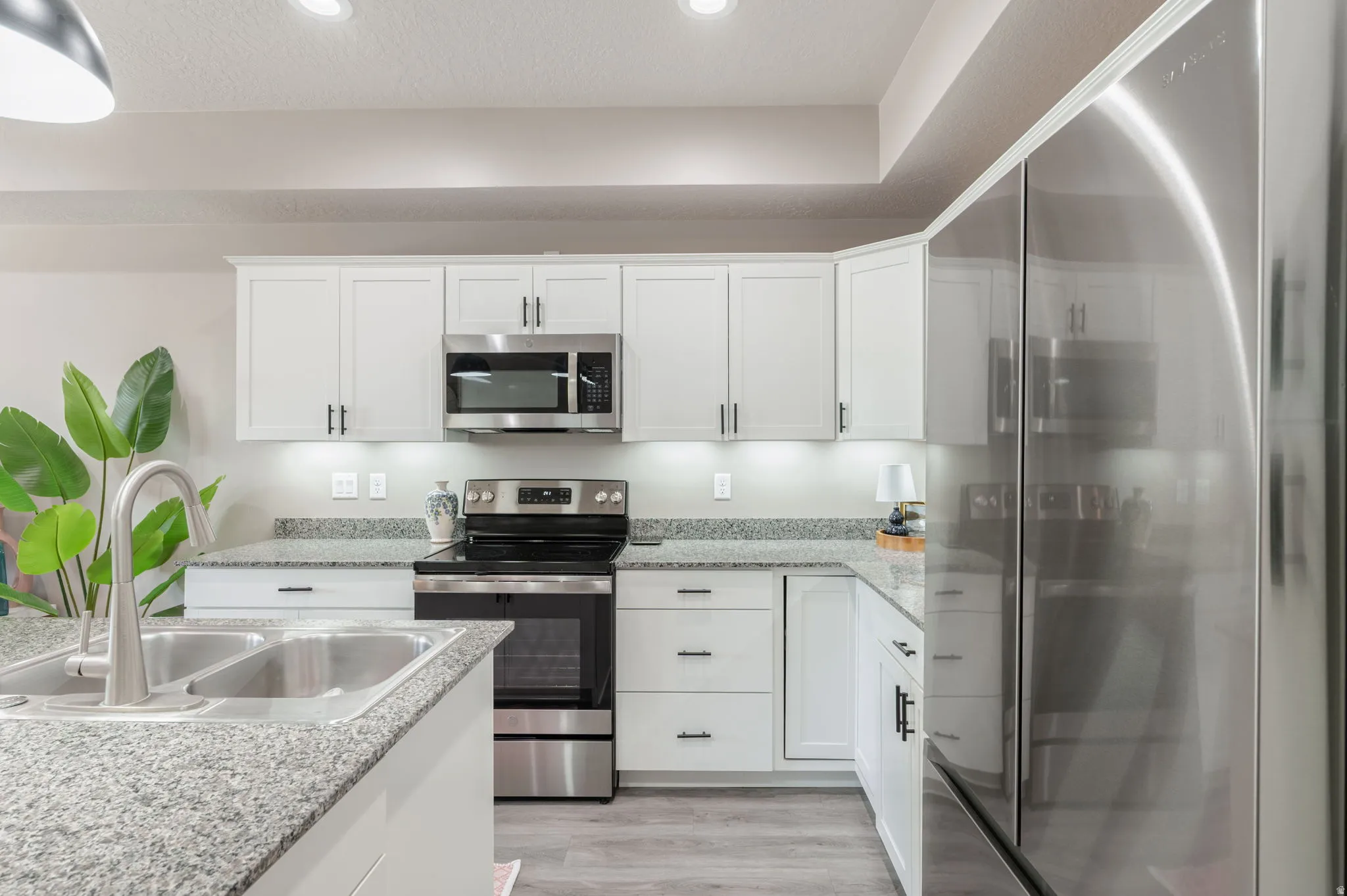 Modern kitchen featuring white cabinetry, stainless steel appliances, granite countertops, and wood-finish flooring