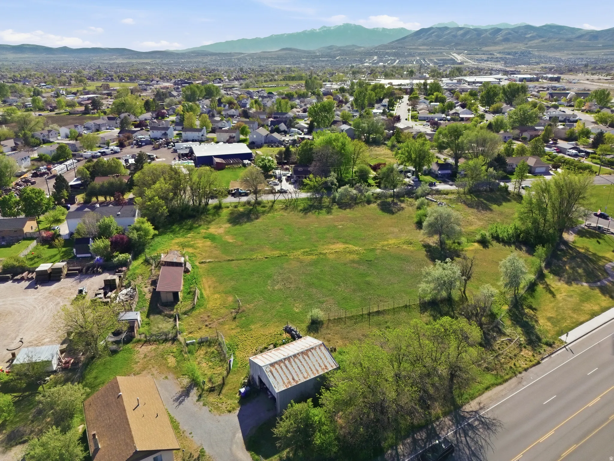 Expansive undeveloped parcel featuring a green grass field, mature trees, mountain range backdrop, and direct road frontage