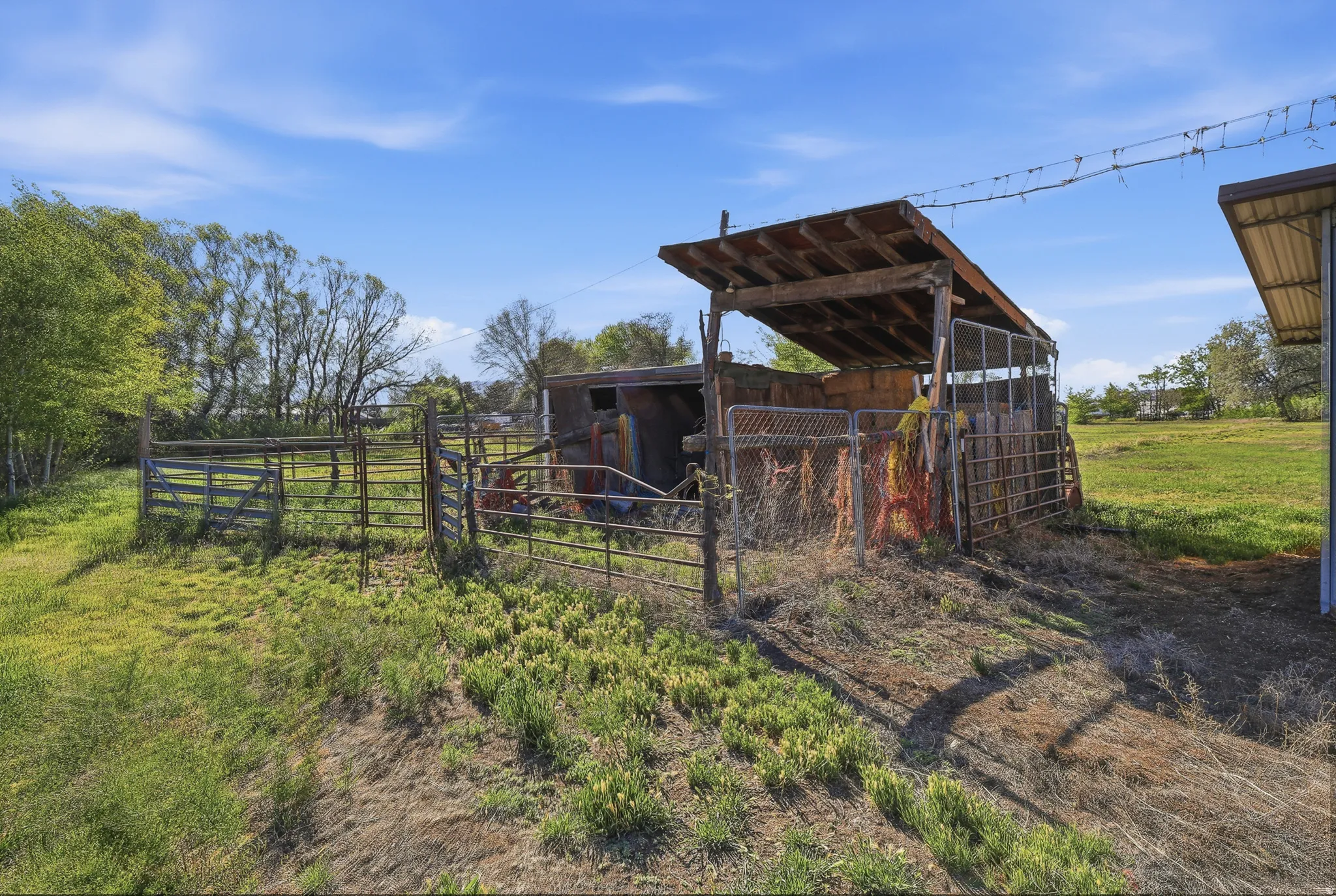 Agricultural outbuilding featuring a sloped wooden roof, metal fencing, and open field space