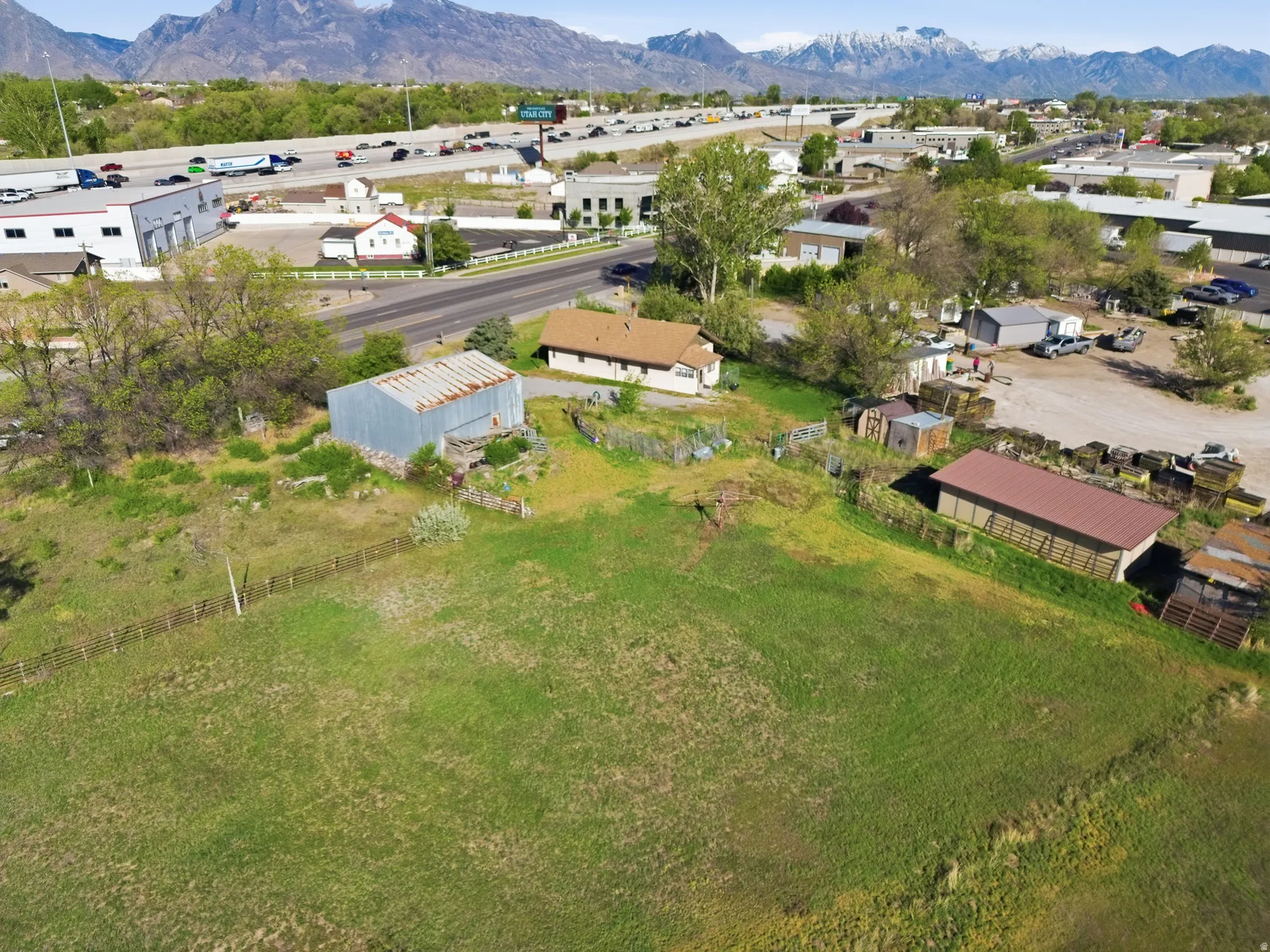 Expansive green space featuring a wood fence, a metal-sided barn, and a separate structure with a reddish-brown roof
