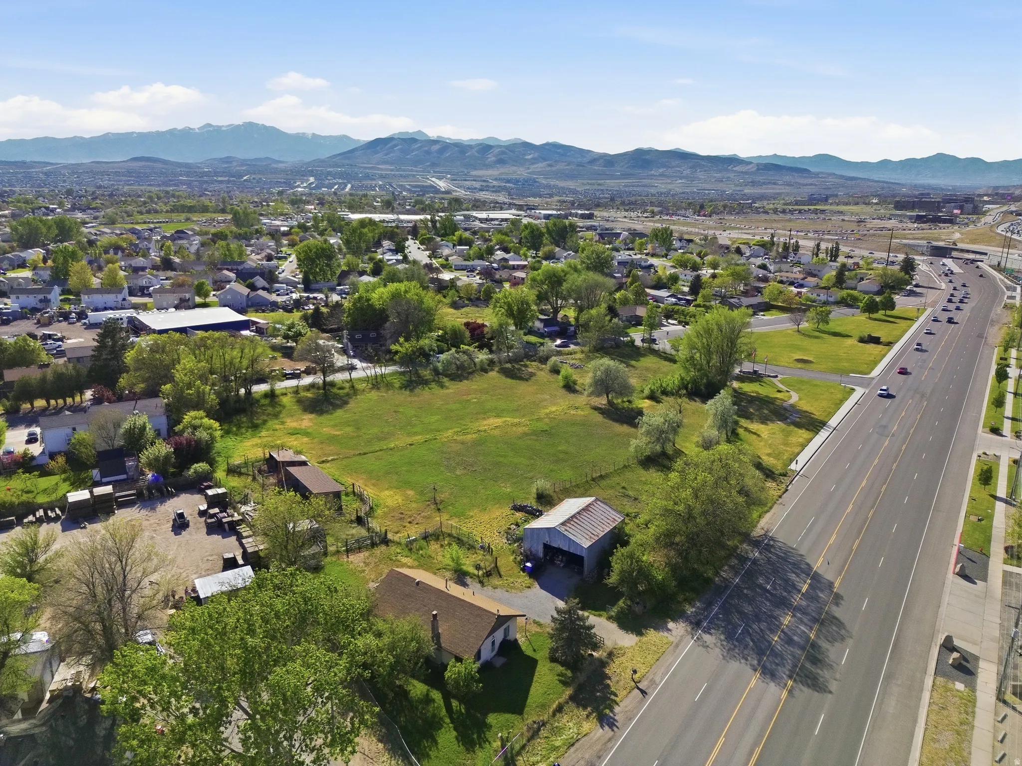 Expansive lot featuring a single-story residence with a brown shingle roof, a detached metal-sided outbuilding, and a large open field