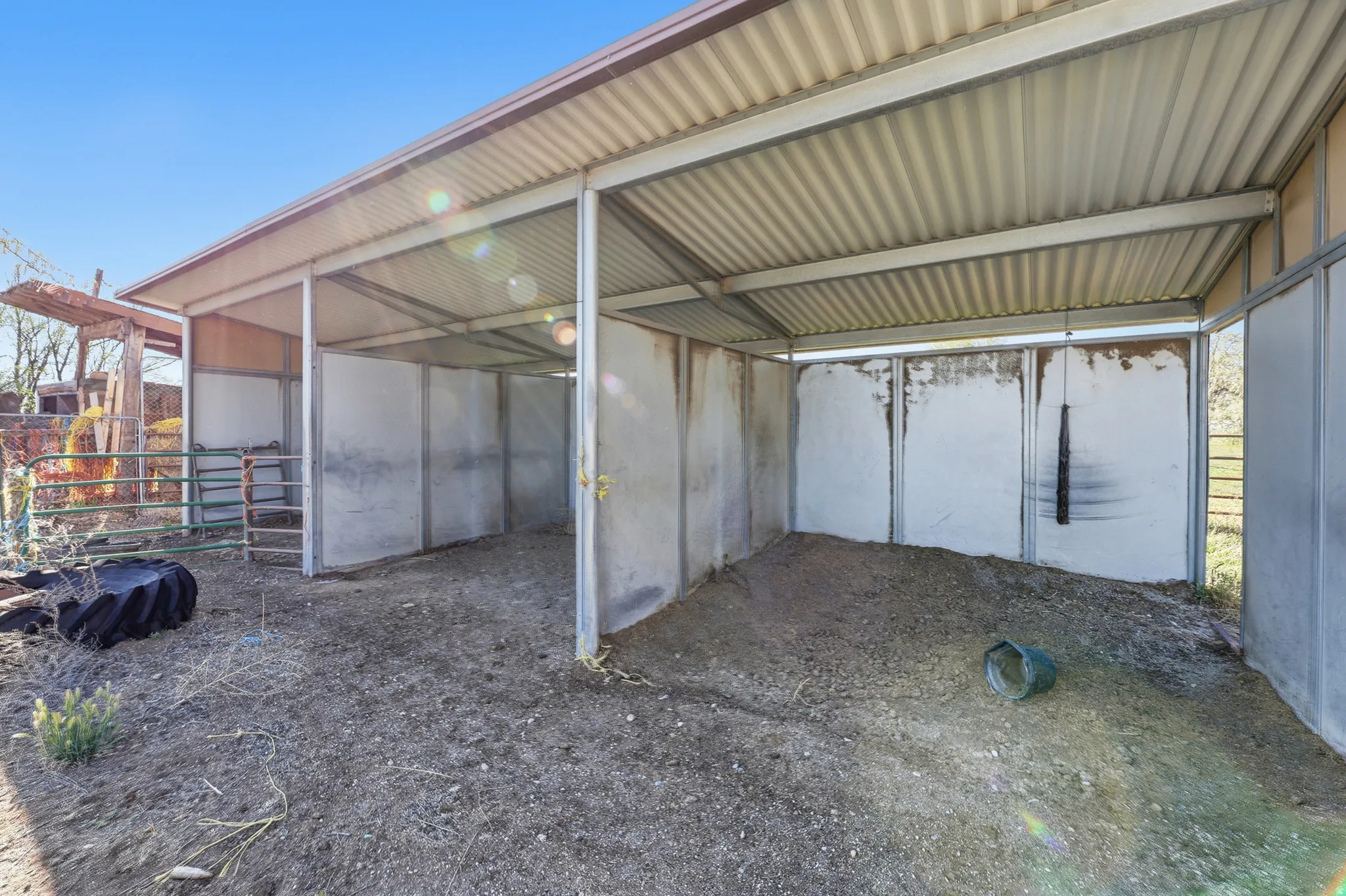 Metal-framed shelter structure featuring a corrugated roof, multiple covered bays, and partial side enclosures