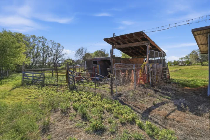 Agricultural outbuilding featuring a sloped wooden roof, metal fencing, and open field space