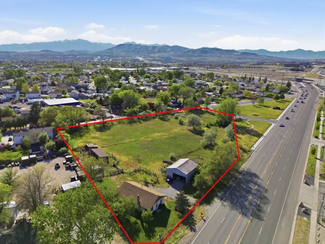Expansive acreage featuring a primary residence, two outbuildings, a substantial grassy area, mature trees, and direct road frontage