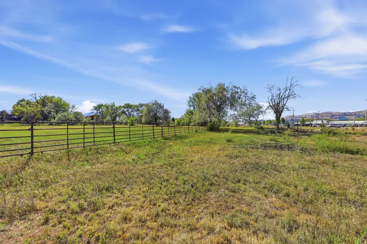 Expansive open field featuring a partial metal fence and varied natural vegetation under a clear blue sky