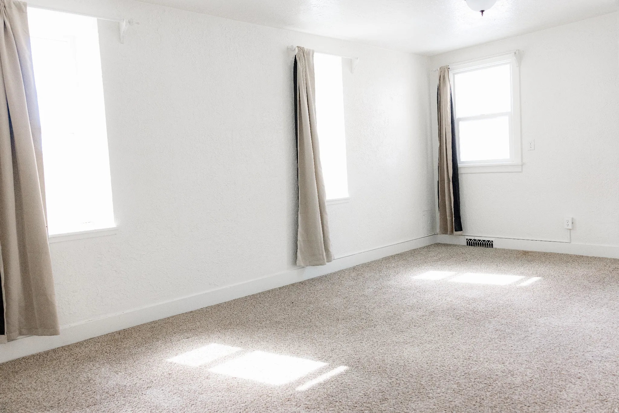 Spacious room featuring light-colored carpeting and white textured walls