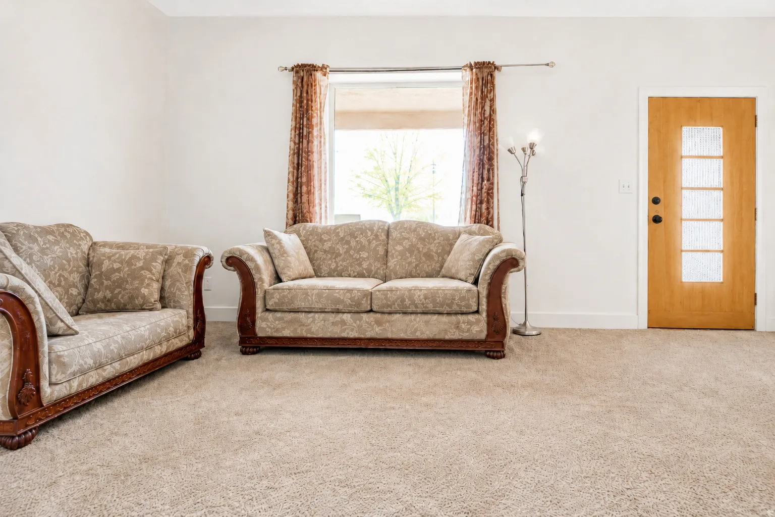 Spacious interior featuring neutral carpeting, a large window with natural light, and a light wood-finish entry door with frosted glass panels