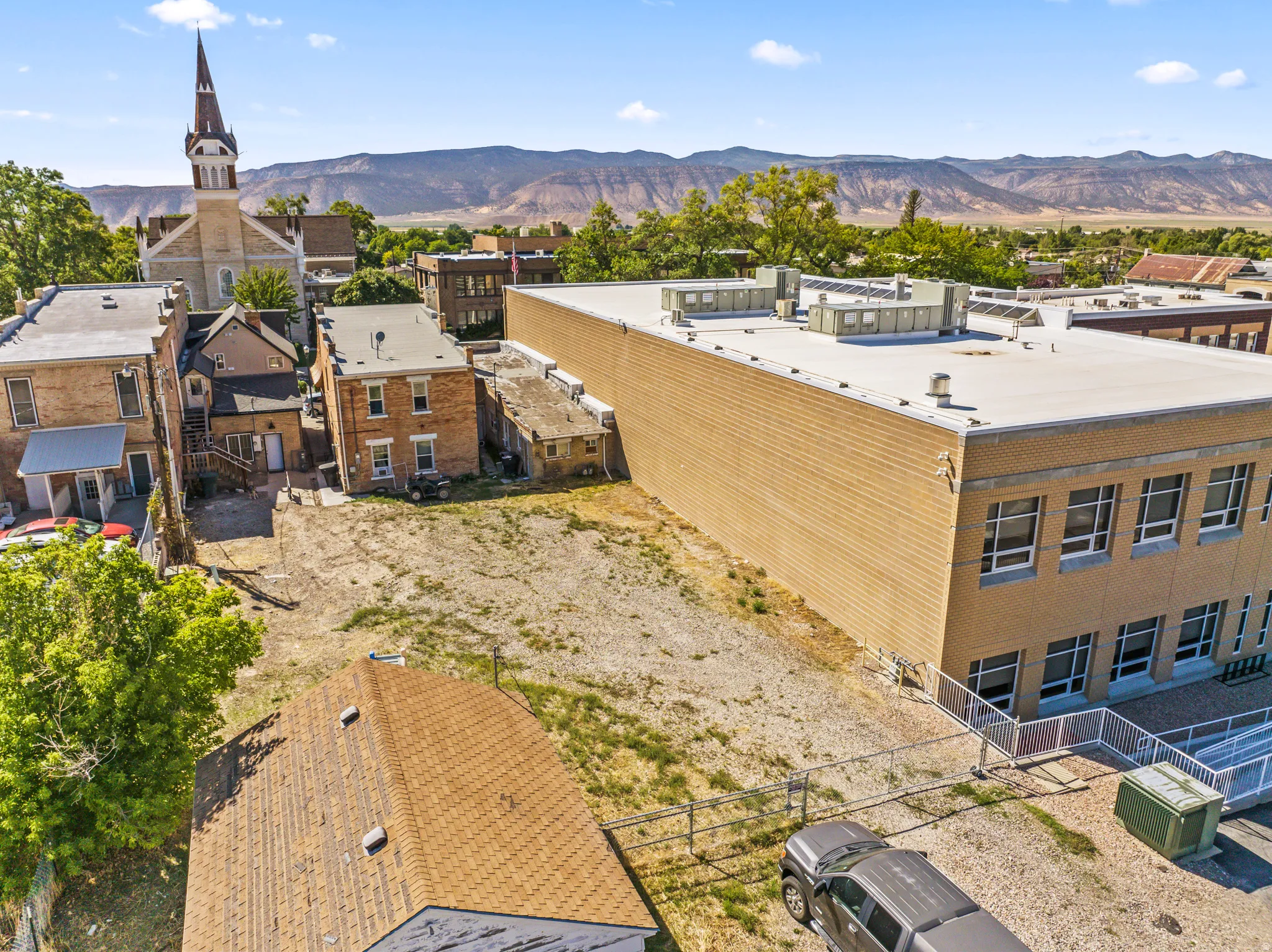 Expansive undeveloped lot with surrounding structures, featuring an adjacent brick building with multiple windows and a flat roof